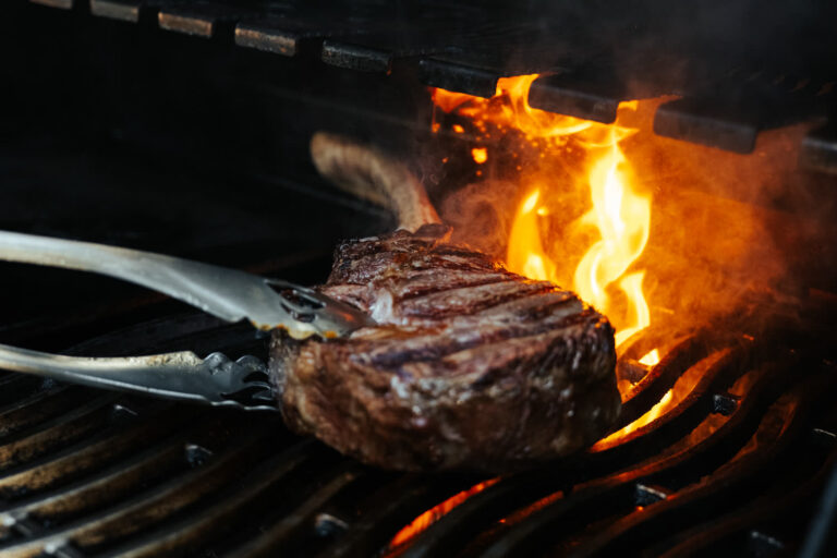 Steak mit Grillstreifen wird mit einer Zange über offener Flamme gewendet